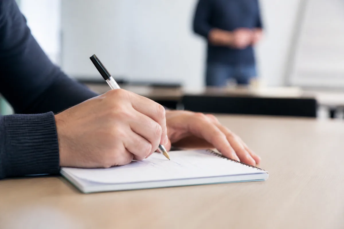 Mains d’adulte prenant des notes dans un cahier à spirale sur une table de formation
